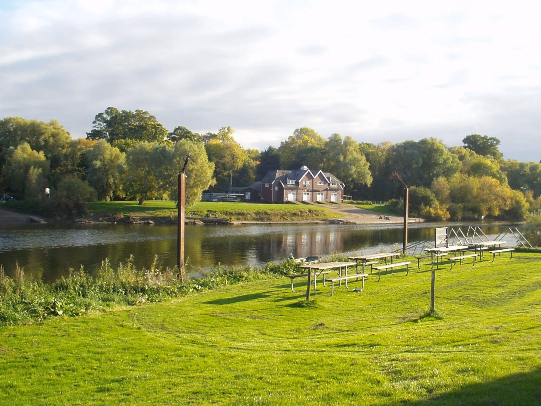 The green Lower Lode camping lawn beside the River Severn with picnic tables at the water's edge.