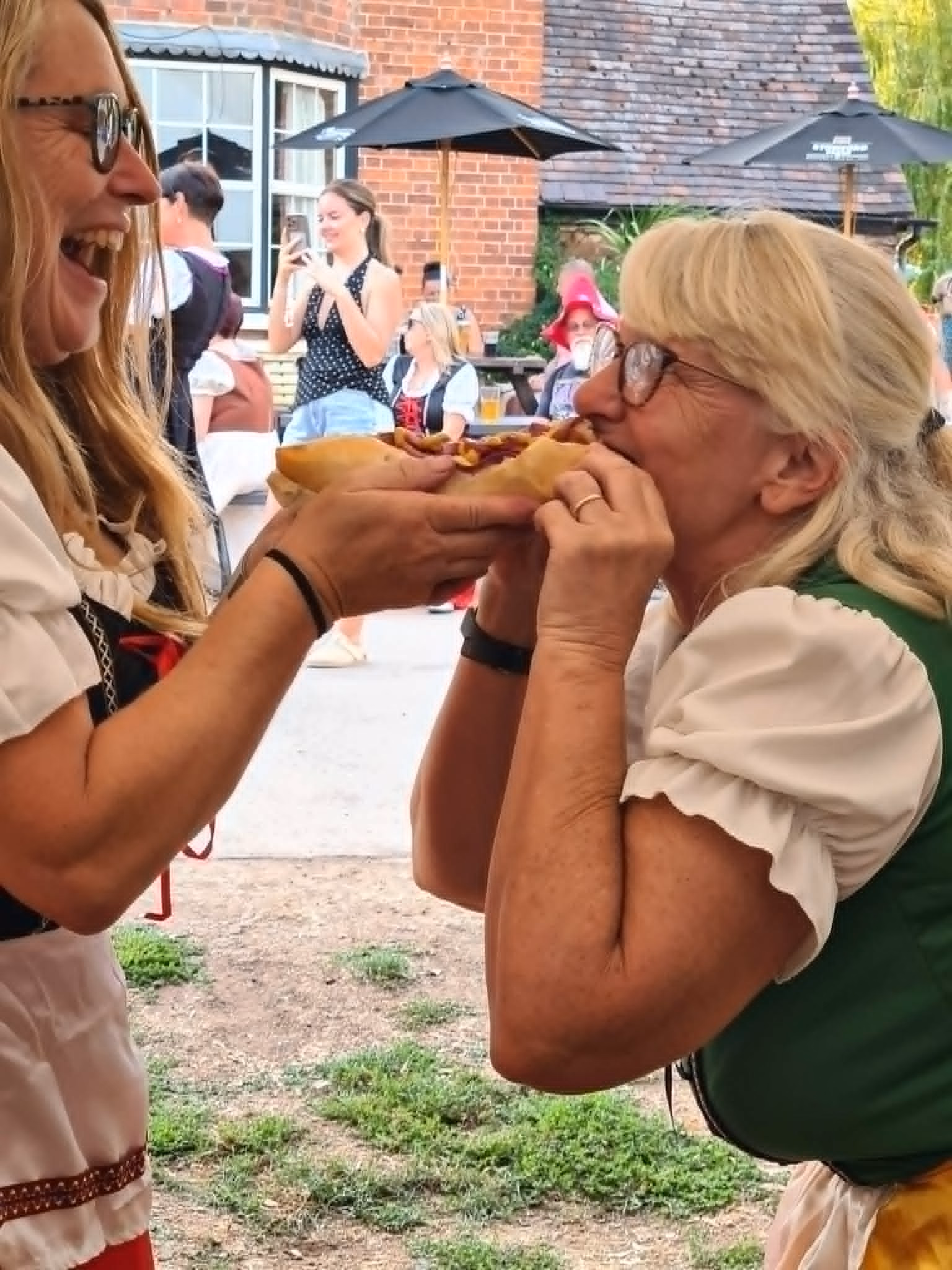 Two visitors in Bavarian-style outfits laughing together beneath the festival marquee.
