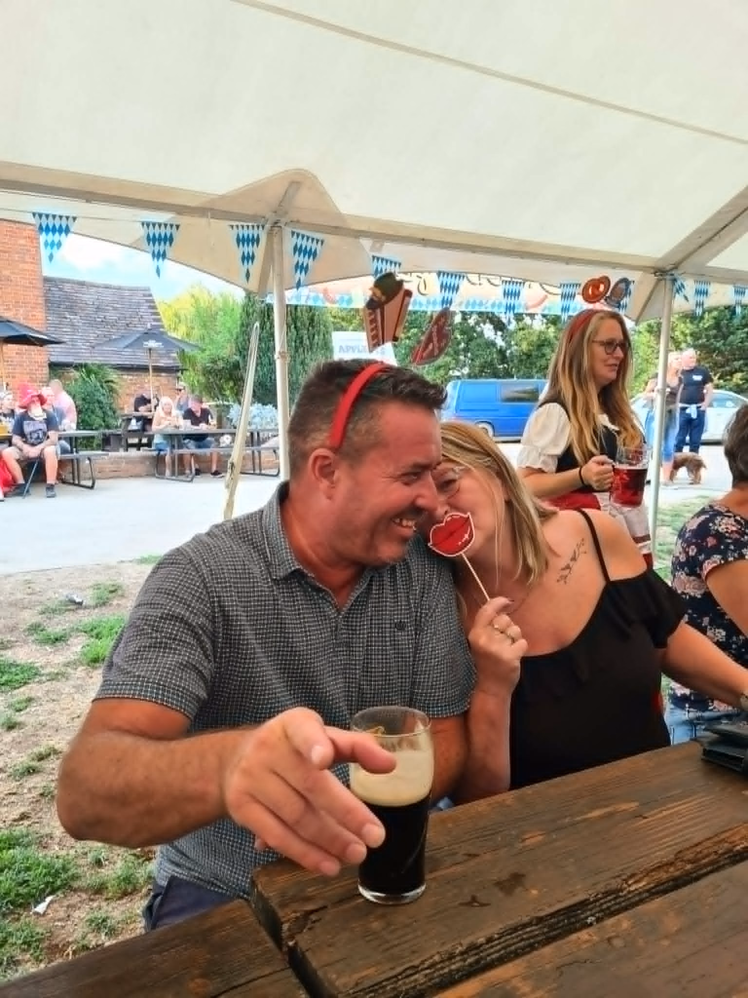 Two visitors laughing together at a picnic table beneath the festival marquee.