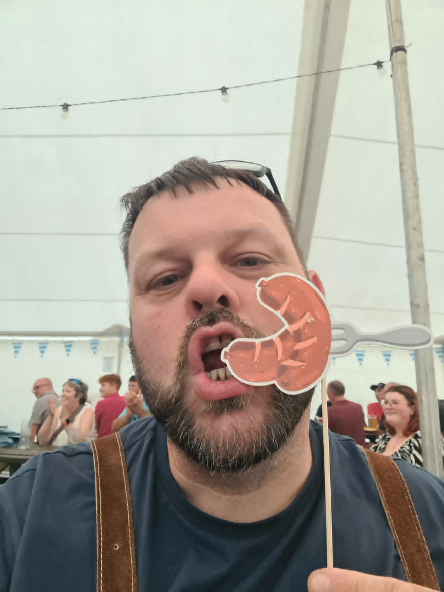 A visitor posing with a novelty sausage photo prop beneath Bavarian bunting.